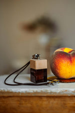 Άρωμα αυτοκινήτου Bellini BY VELCHEVA 10ml σε γυάλινο μπουκάλι amber με ξύλινο καπάκι και δερμάτινο κορδόνι, δίπλα σε φρέσκο ροδάκινο