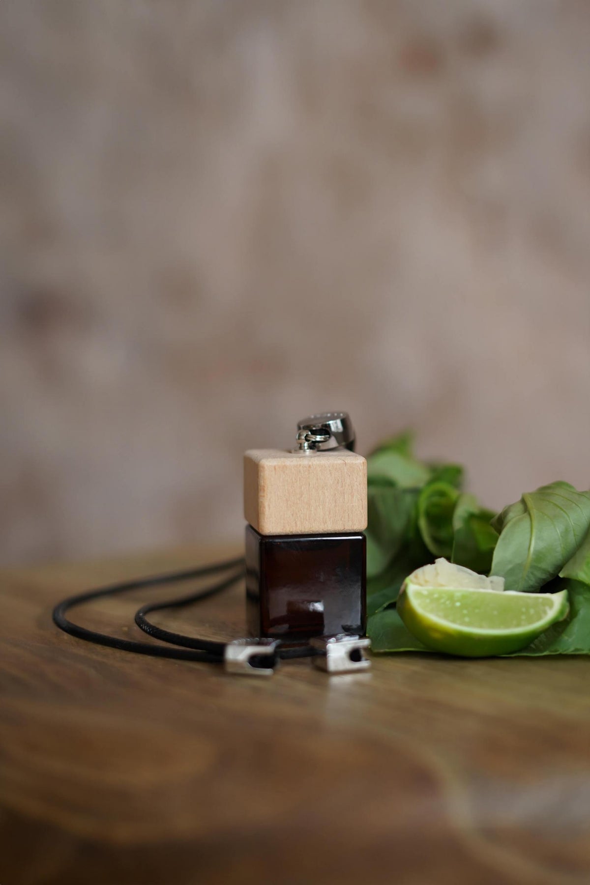 Άρωμα αυτοκινήτου Lime Basil BY VELCHEVA 10ml σε γυάλινο μπουκάλι amber με ξύλινο καπάκι και μαύρο κορδόνι, δίπλα σε λάιμ και φύλλα βασιλικού