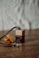 Άρωμα αυτοκινήτου Salted Caramel BY VELCHEVA 10ml σε γυάλινο μπουκάλι amber με ξύλινο καπάκι και μαύρο κορδόνι, δίπλα σε καραμέλες