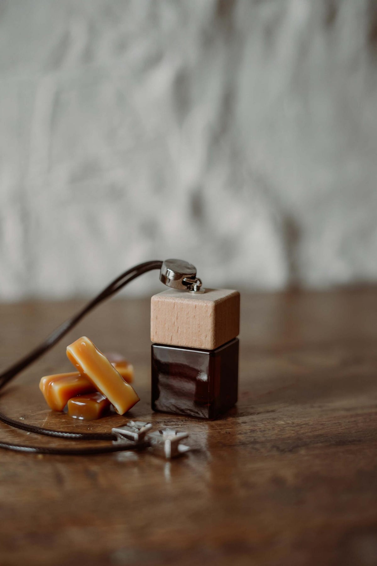 Άρωμα αυτοκινήτου Salted Caramel BY VELCHEVA 10ml σε γυάλινο μπουκάλι amber με ξύλινο καπάκι και μαύρο κορδόνι, δίπλα σε καραμέλες
