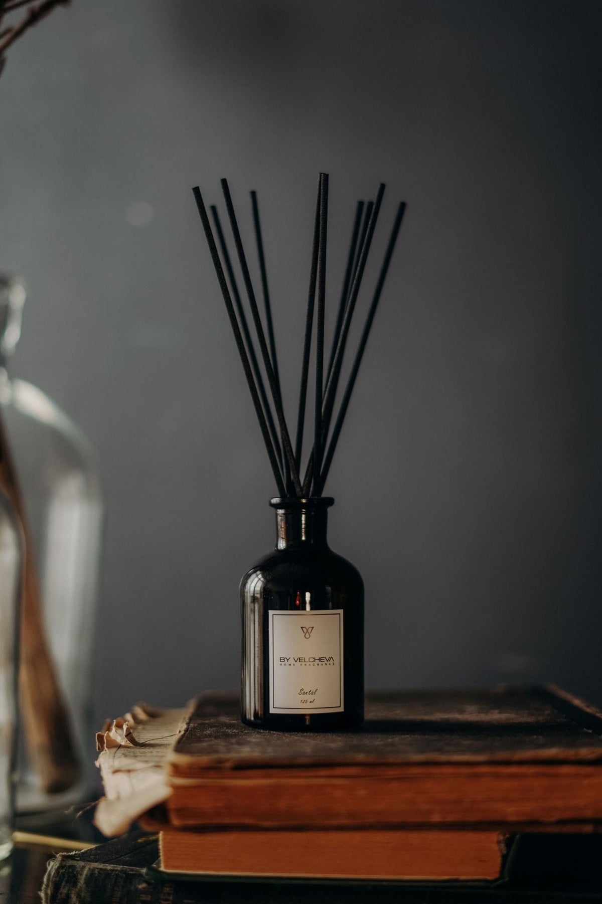 Αρωματικό χώρου με στικ Santal BY VELCHEVA σε μαύρο γυάλινο μπουκάλι πάνω σε παλιά βιβλία, με ξύλινο, ζεστό φόντο 125 ml