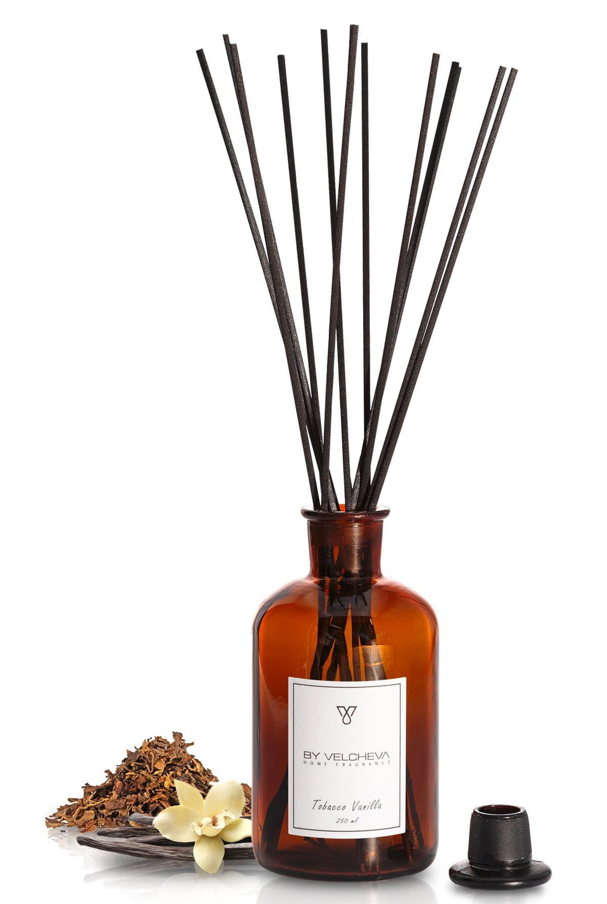 Αρωματικό χώρου με στικ Tobacco Vanilla BY VELCHEVA σε καφέ γυάλινο μπουκάλι με φύλλα καπνού και άνθος βανίλιας, σε λευκό φόντο
