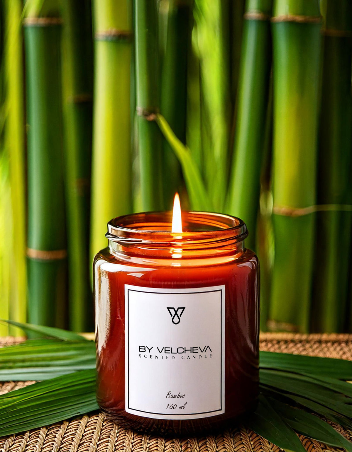 Αρωματικό κερί Bamboo BY VELCHEVA 160ml σε γυάλινο βάζο amber, αναμμένο, με φόντο πράσινα καλάμια μπαμπού