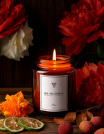 Αρωματικό κερί Fleur BY VELCHEVA 160ml σε γυάλινο βάζο amber, αναμμένο, με κόκκινες παιώνιες, φέτες λάιμ και λίτσι