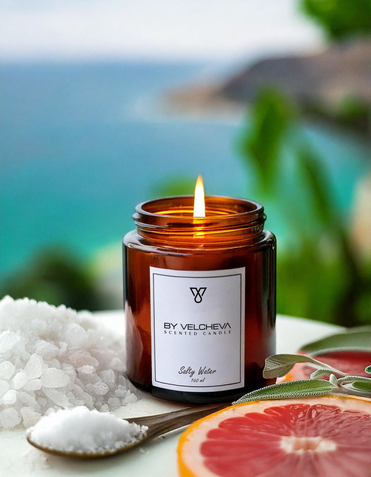 Αρωματικό κερί Salty Water BY VELCHEVA 160ml σε γυάλινο βάζο amber, αναμμένο, με θαλασσινό αλάτι και γκρέιπφρουτ, με φόντο θάλασσα

