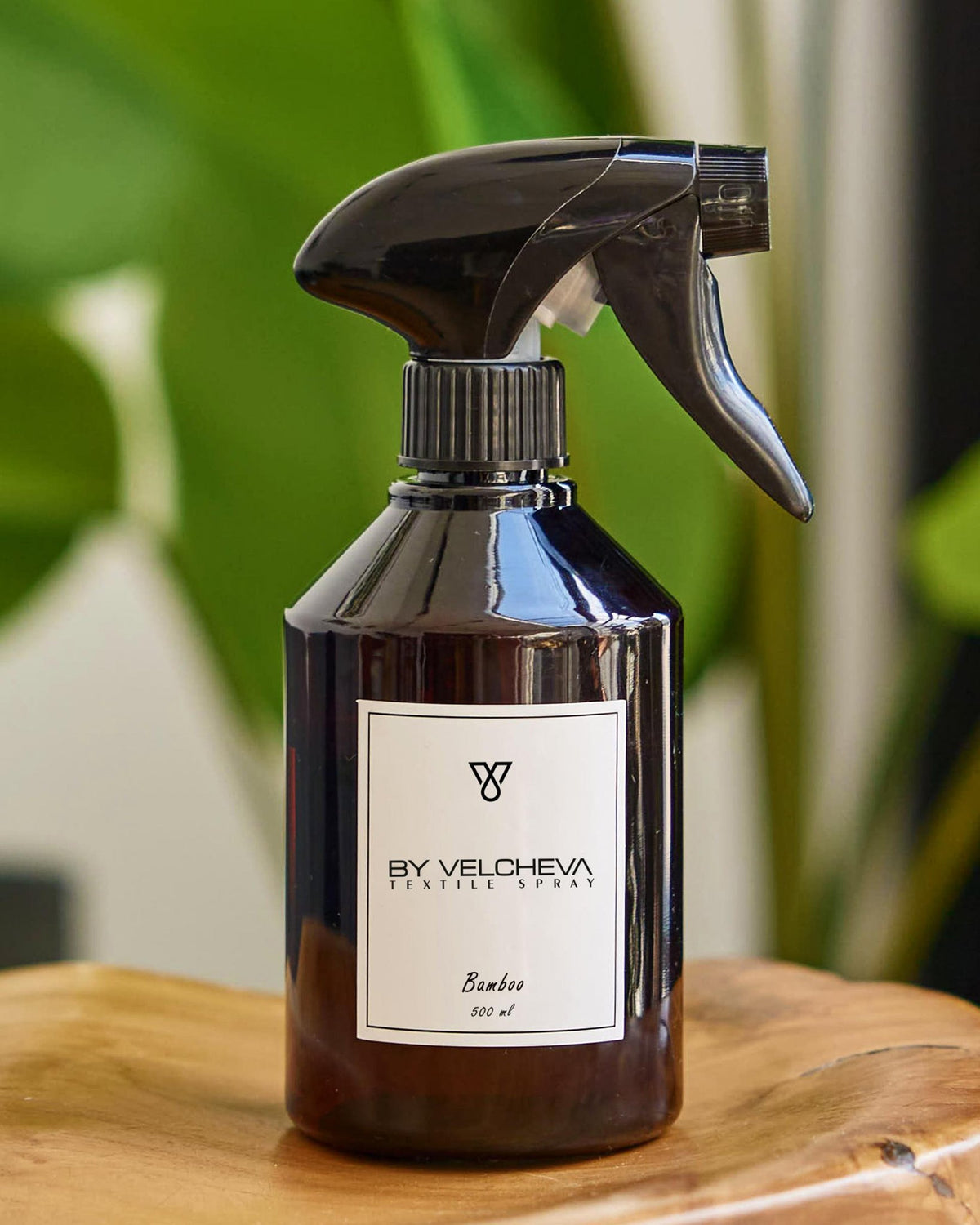 Αρωματικό σπρέι υφασμάτων Bamboo BY VELCHEVA 500ml σε καφέ μπουκάλι με αντλία ψεκασμού, με φόντο πράσινα φυτά