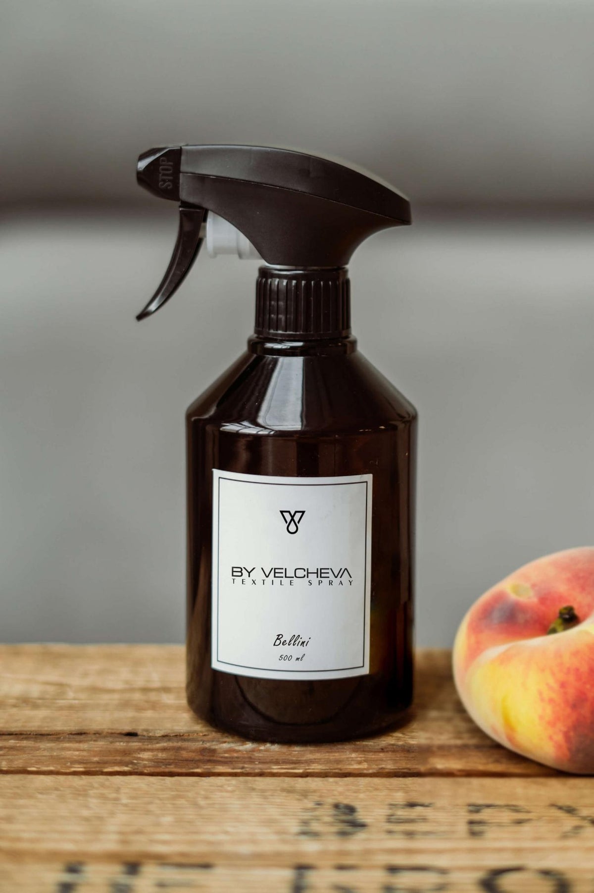 Αρωματικό σπρέι υφασμάτων Bellini BY VELCHEVA 500ml σε καφέ μπουκάλι με αντλία ψεκασμού, δίπλα σε φρέσκο ροδάκινο