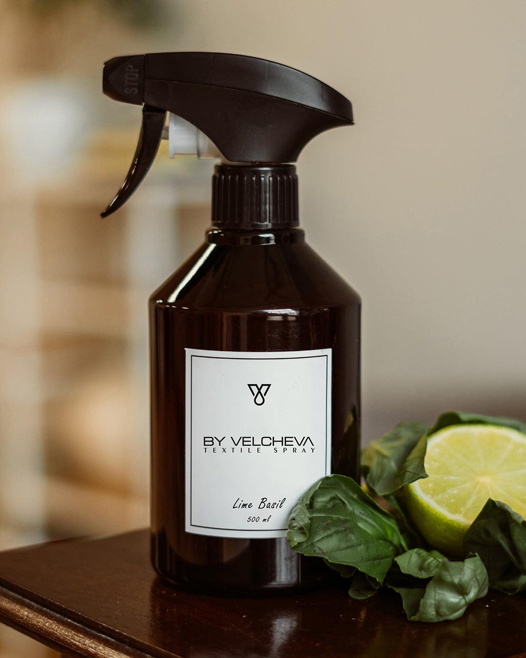 Αρωματικό σπρέι υφασμάτων Lime Basil BY VELCHEVA 500ml σε καφέ μπουκάλι με αντλία ψεκασμού, δίπλα σε μισό λάιμ και φύλλα βασιλικού
