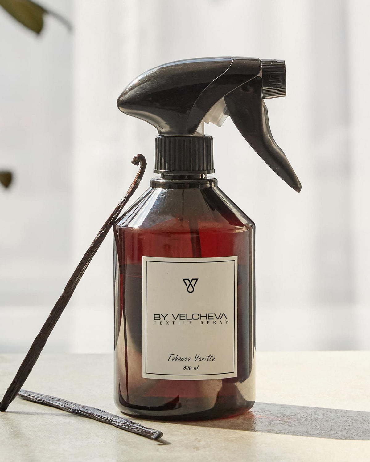 Αρωματικό σπρέι υφασμάτων Tobacco Vanilla BY VELCHEVA 500ml σε καφέ μπουκάλι με αντλία ψεκασμού, δίπλα σε λοβούς βανίλιας