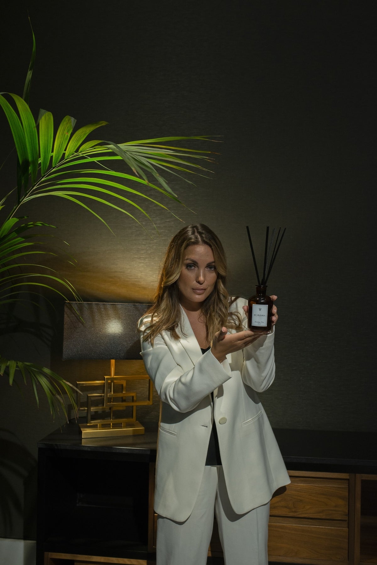 Γυναίκα κρατά αρωματικό reed diffuser ByVelcheva σε κομψό βραδινό σαλόνι